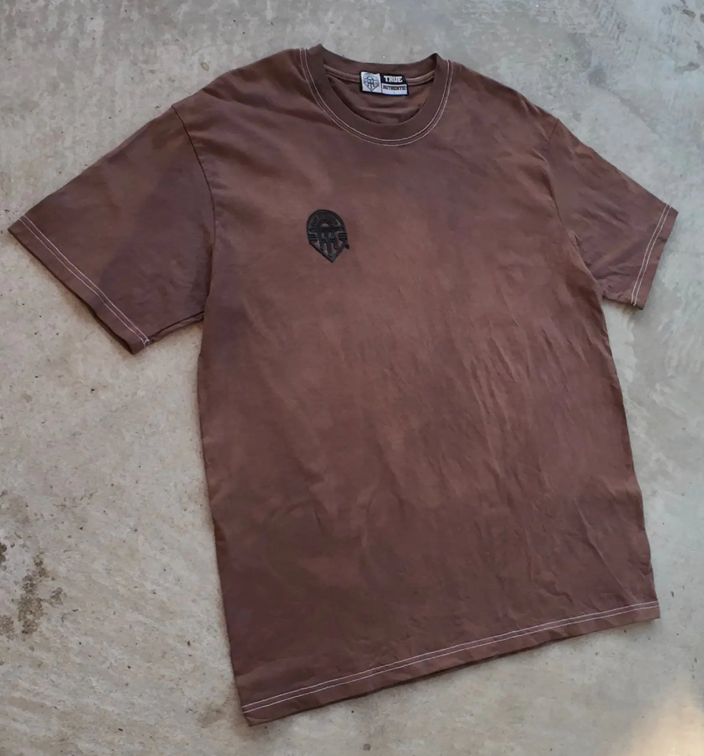 Brown t-shirt with a logo on a concrete floor