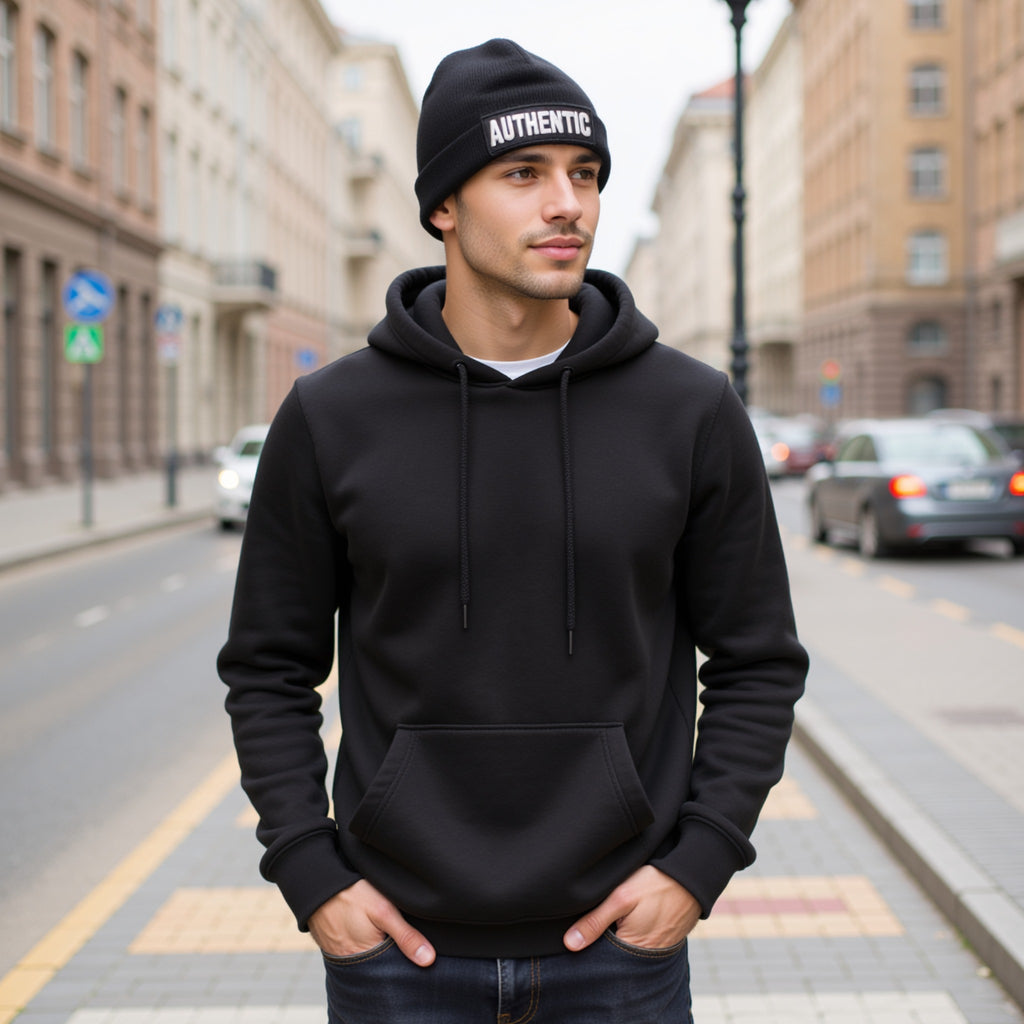 Man wearing a black hoodie and beanie with 'AUTHENTIC' text on a city street.