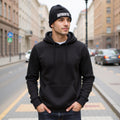 Man wearing a black hoodie and beanie with 'AUTHENTIC' text on a city street.