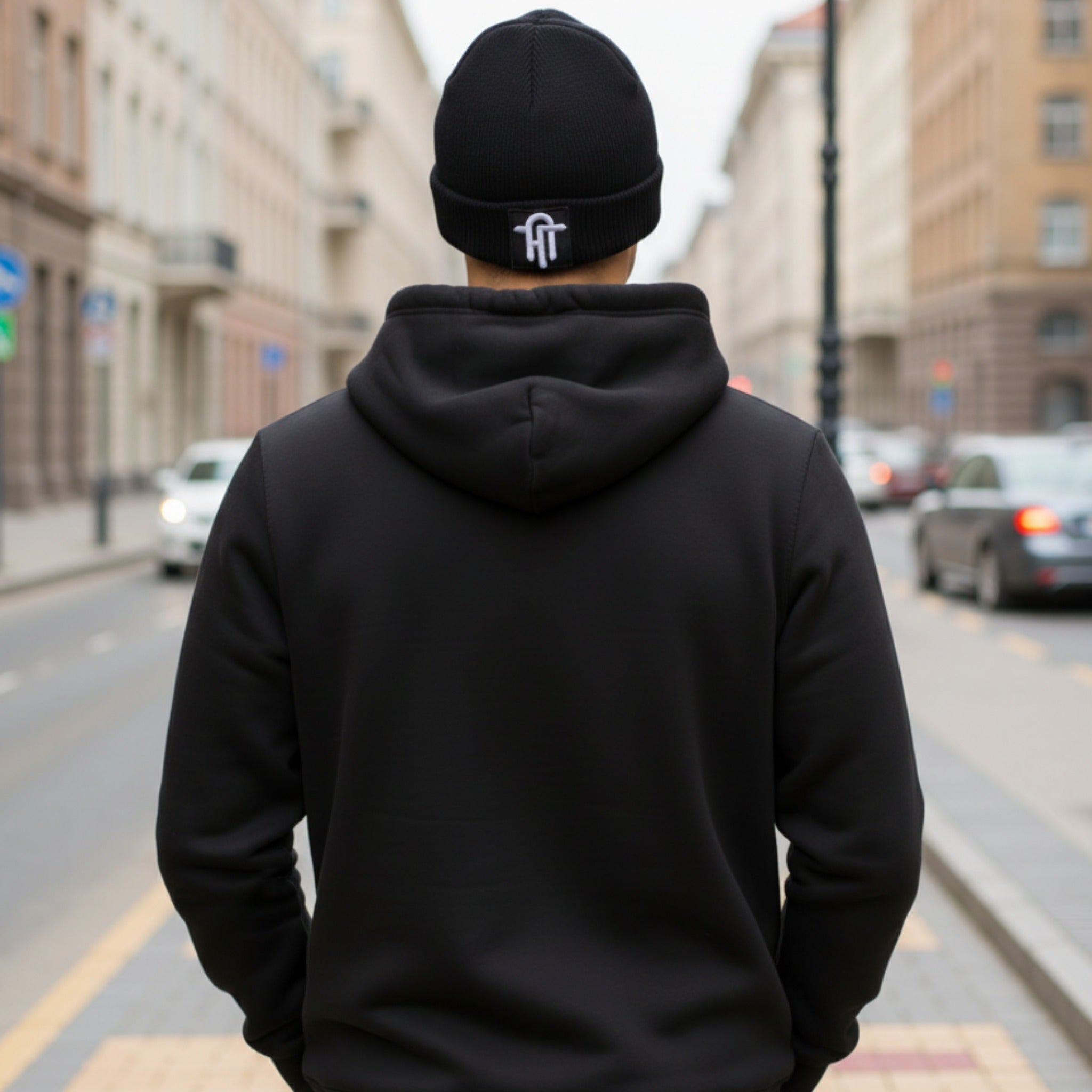 Person wearing a black hoodie and beanie with a logo on a city street