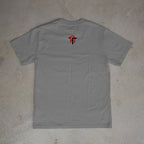 Gray t-shirt with a logo on the back, placed on a textured surface.