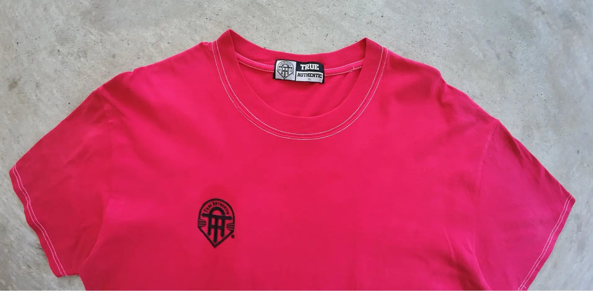 Pink t-shirt with a black logo on a gray surface