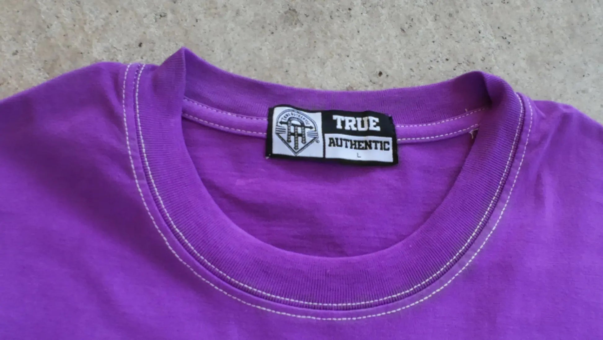 Purple shirt with a 'TRUE AUTHENTIC' label on a concrete surface