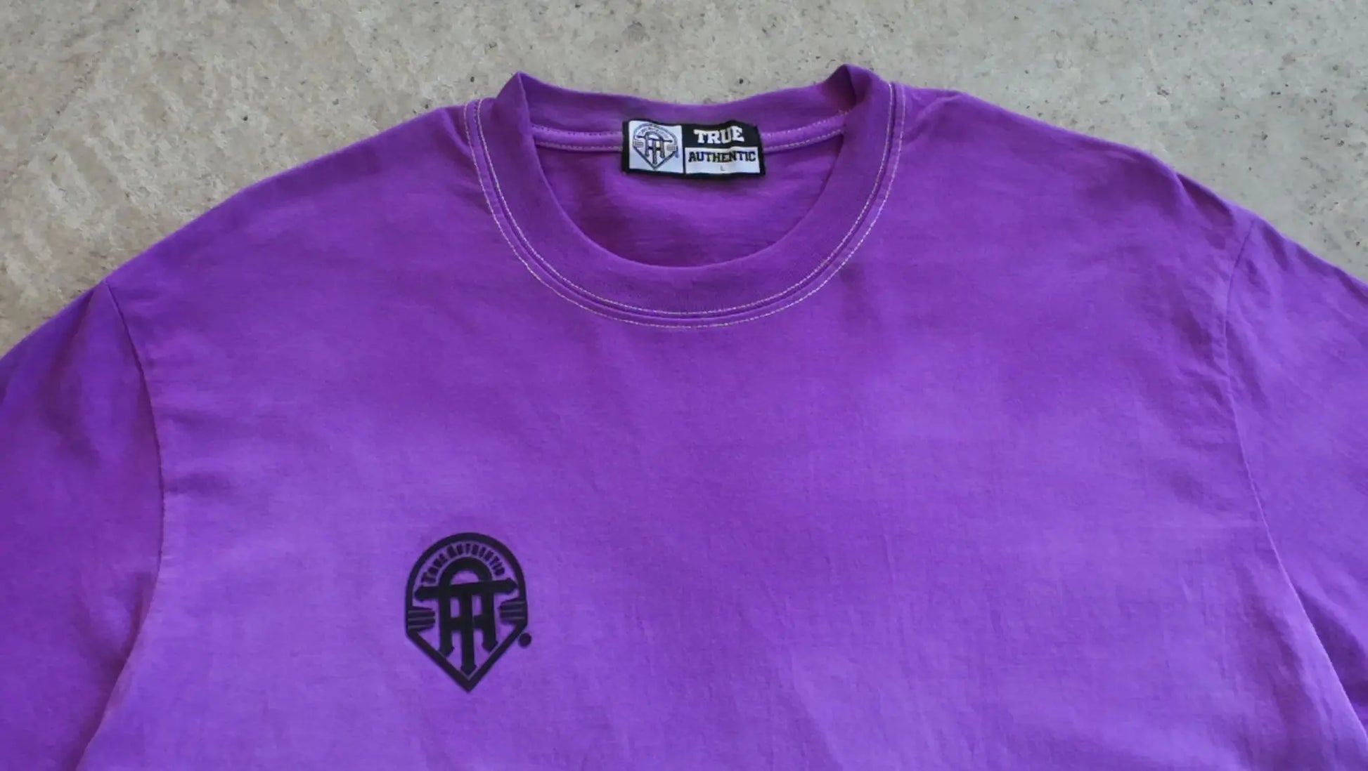 Purple shirt with a logo on a gray surface