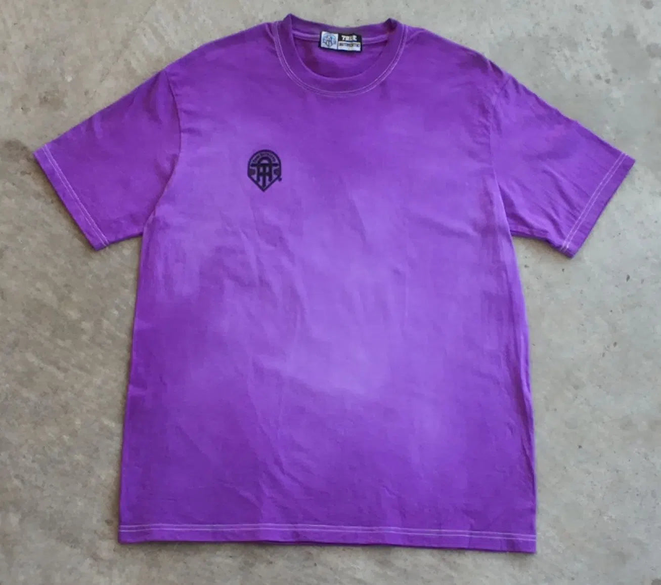 Purple t-shirt with a black logo on a beige surface