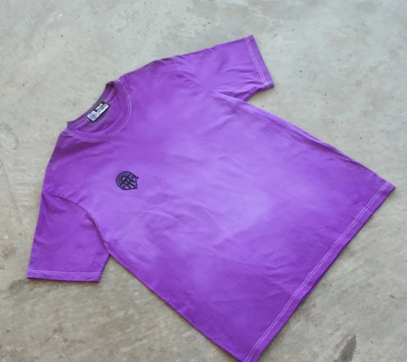 Purple t-shirt with a logo on a concrete floor