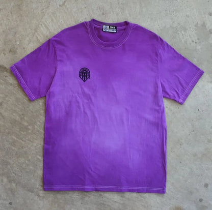 A purple t-shirt with a small logo on a concrete floor