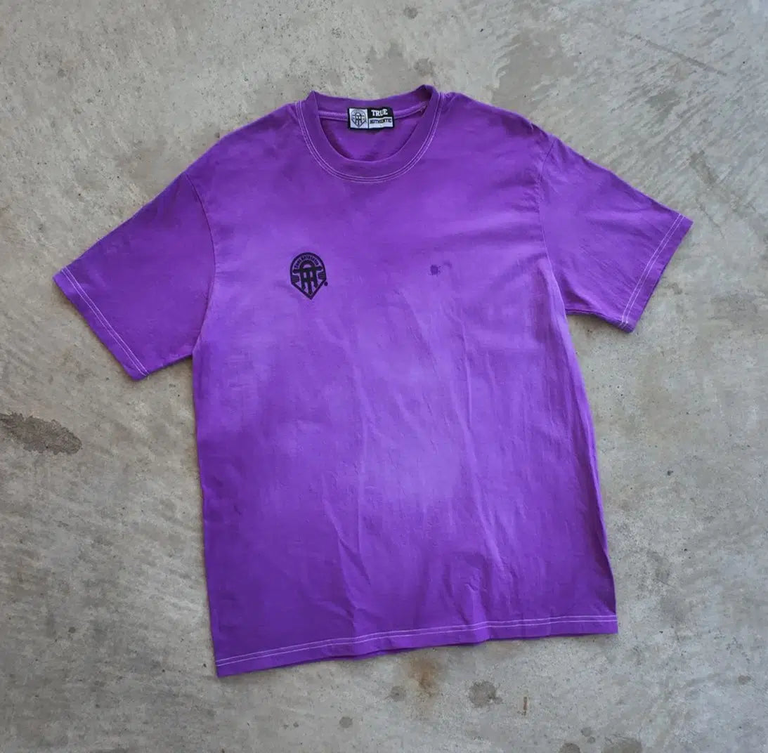 Purple t-shirt with a small logo on a concrete floor