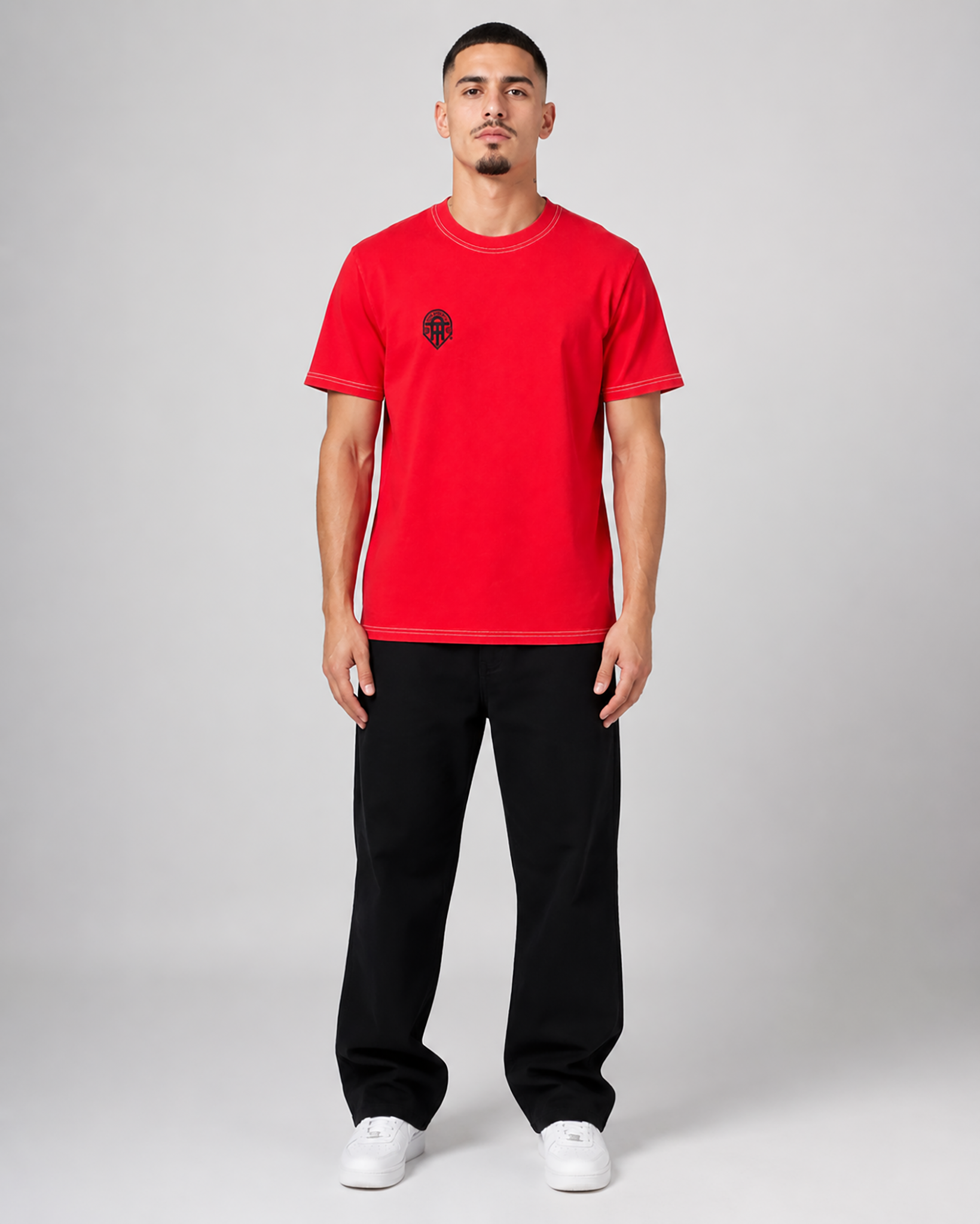 Person wearing a red t-shirt with a black logo and black pants on a white background