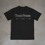 Black t-shirt with 'Trust the Process' text on a beige surface