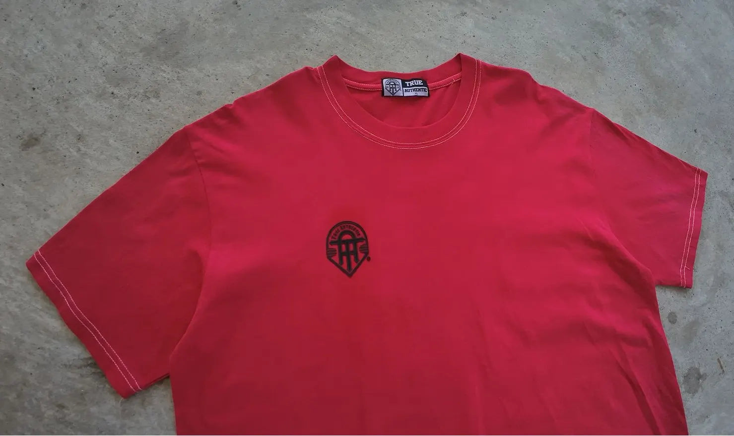 Red t-shirt with a black logo on a gray surface