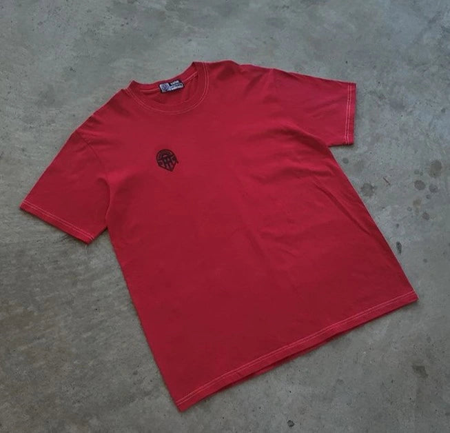 Red t-shirt with a small logo on a concrete floor