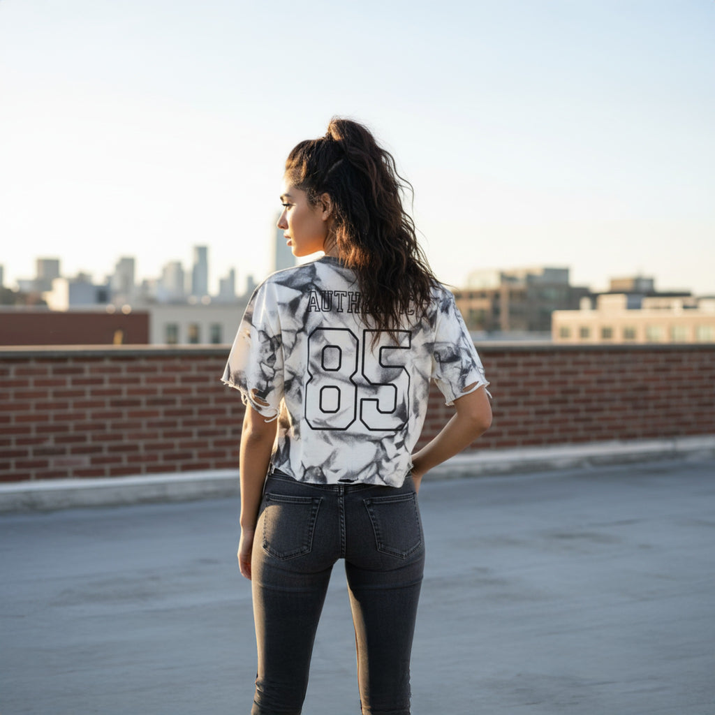 Person wearing a patterned shirt and jeans on a rooftop with city skyline in the background