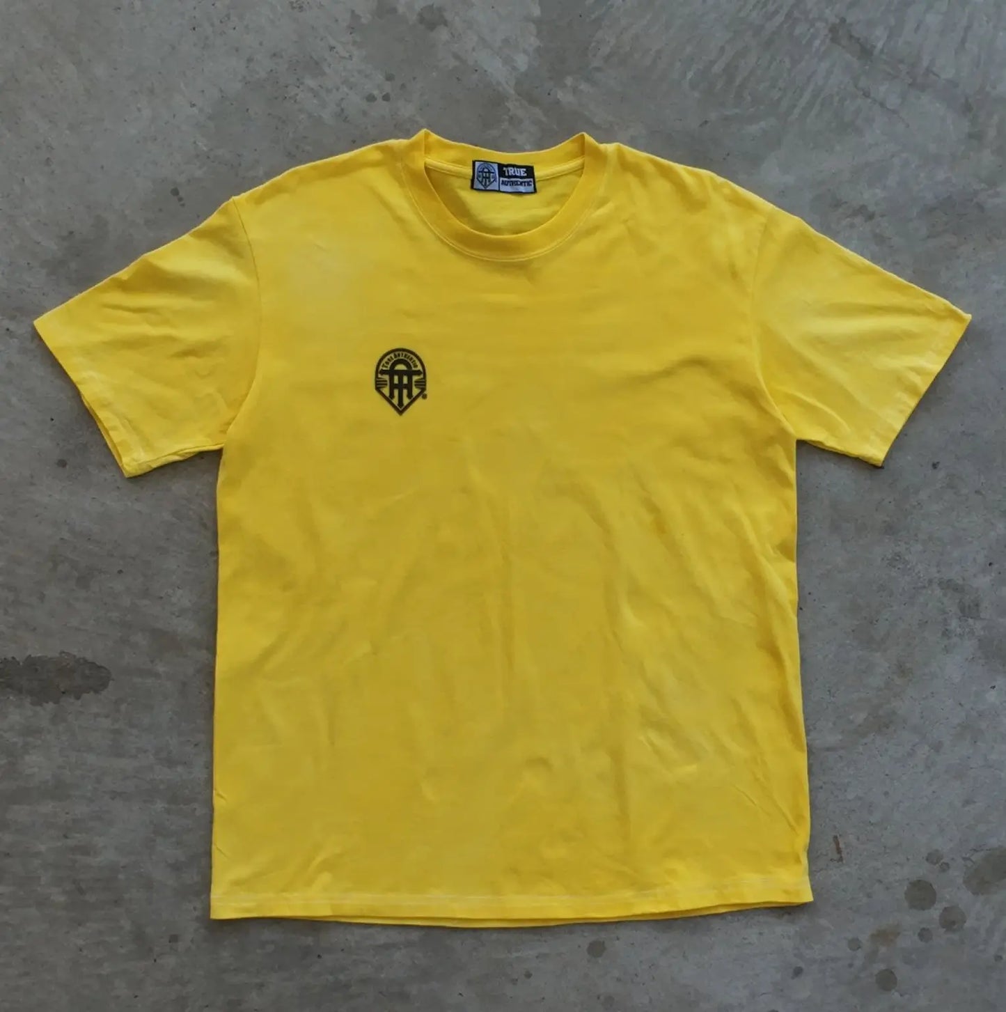 Yellow t-shirt with a black logo on a gray concrete surface