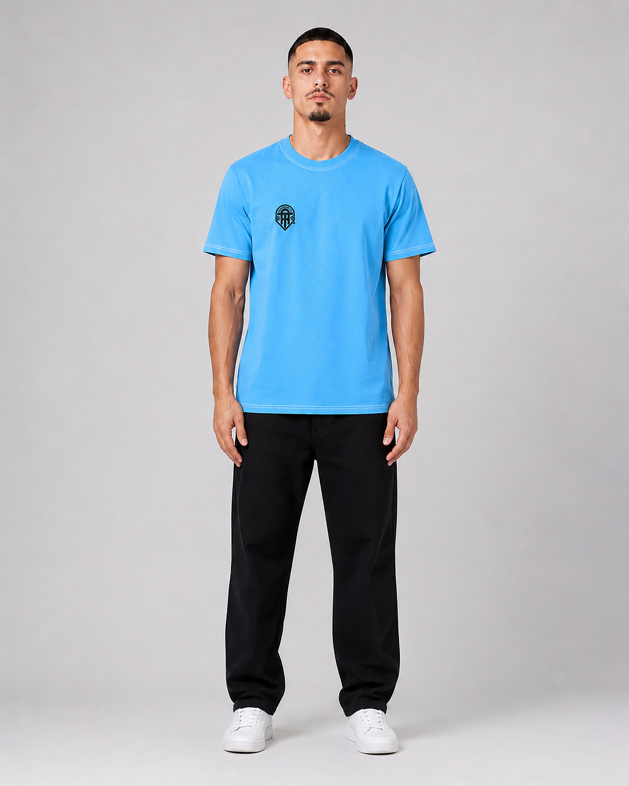Man wearing a blue t-shirt with a logo and black pants on a gray background
