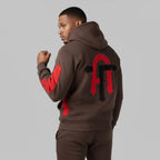Man wearing a brown hoodie with red and black designs on the back against a gray background