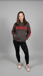 Person wearing a gray hoodie with red sleeves and text, black leggings, and white sneakers on a gray background