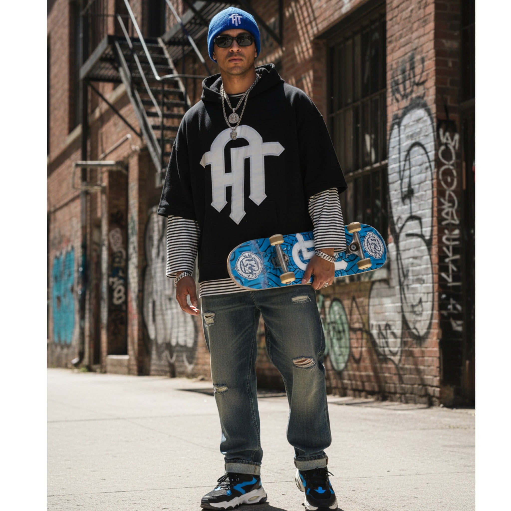 Person holding a skateboard in an urban setting with graffiti on the wall.